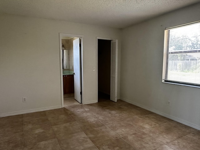 1433 SW San Esteban Ave, Port Saint Lucie, FL 34953 - unfurnished bedroom featuring a textured ceiling, ensuite bath, a closet, and baseboards