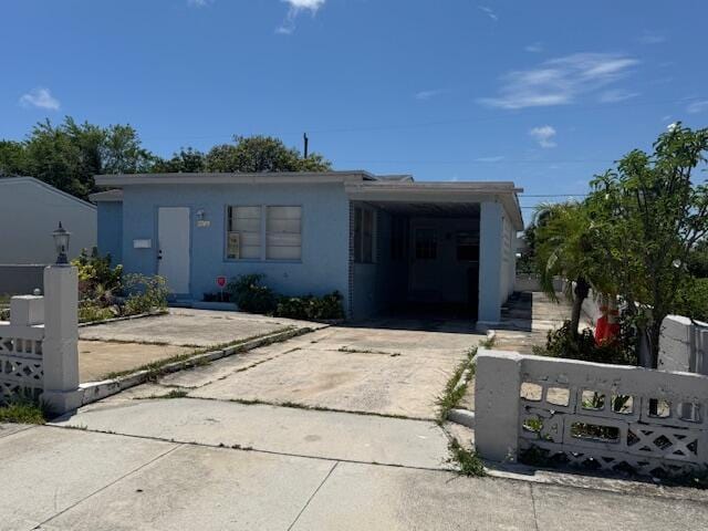 view of front of house with a fenced front yard, concrete driveway, stucco siding, and a carport