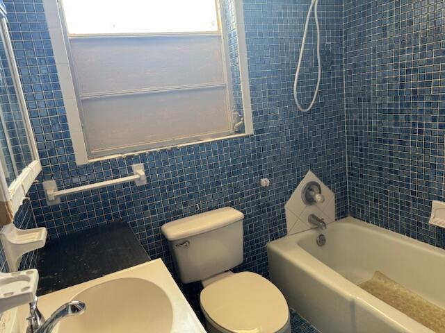 bathroom featuring a sink, tub / shower combination, tile walls, and toilet