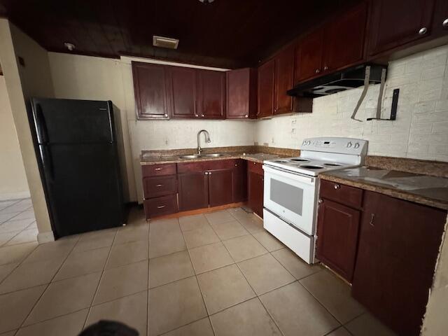 kitchen with electric stove, freestanding refrigerator, under cabinet range hood, a sink, and reddish brown cabinets