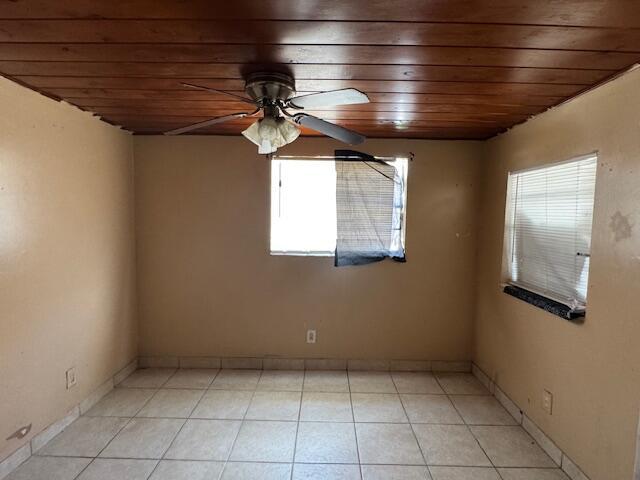 empty room featuring wood ceiling, ceiling fan, light tile patterned flooring, and baseboards