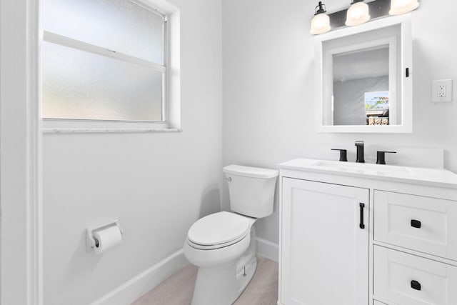 half bathroom featuring toilet, wood finished floors, baseboards, and vanity