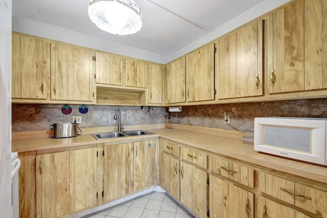 kitchen featuring white microwave, a sink, light countertops, and light tile patterned flooring
