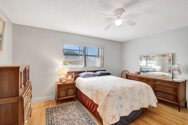 bedroom with light wood-type flooring, a textured ceiling, ceiling fan, and baseboards