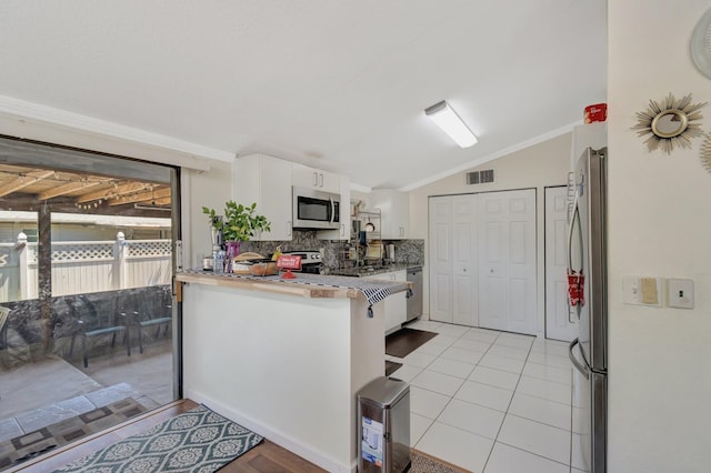 kitchen featuring appliances with stainless steel finishes, vaulted ceiling, a peninsula, white cabinets, and tasteful backsplash