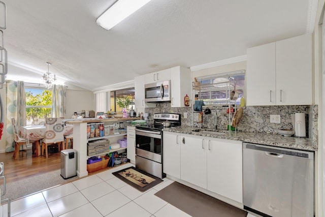 kitchen featuring appliances with stainless steel finishes, healthy amount of natural light, tasteful backsplash, a sink, and vaulted ceiling