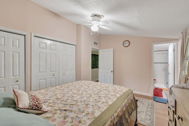 bedroom with a textured ceiling, vaulted ceiling, multiple closets, light wood-type flooring, and ceiling fan