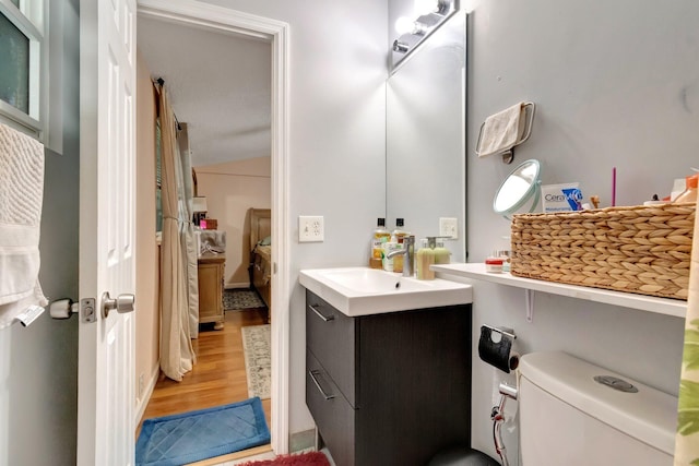 ensuite bathroom with wood finished floors, vanity, vaulted ceiling, and toilet