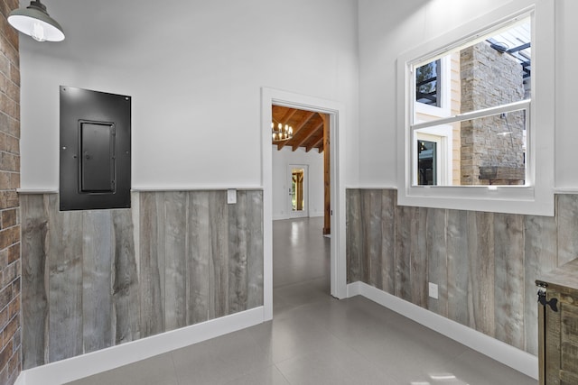 corridor with electric panel, wainscoting, and a chandelier