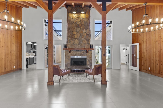 living room with a chandelier, beamed ceiling, a towering ceiling, wooden walls, and a stone fireplace