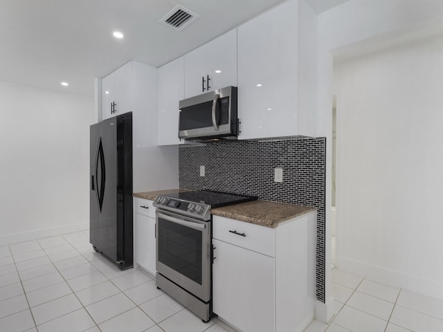 1138 SW Gardena Ave, Port Saint Lucie, FL 34953 - kitchen featuring stainless steel appliances, white cabinetry, backsplash, light tile patterned flooring, and dark countertops
