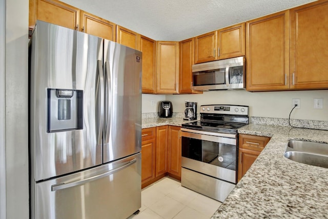 1266 NW 126th Ter, Sunrise, FL 33323 - kitchen with stainless steel appliances, brown cabinets, light stone counters, and a textured ceiling