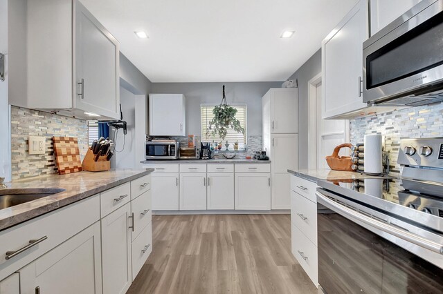2115 SW 22nd St, Boynton Beach, FL 33426 - kitchen featuring stainless steel appliances, tasteful backsplash, light wood-style flooring, light stone counters, and white cabinetry
