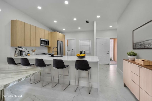 8269 Springtree Rd, Boca Raton, FL 33496 - kitchen featuring appliances with stainless steel finishes, modern cabinets, light brown cabinets, a kitchen bar, and recessed lighting