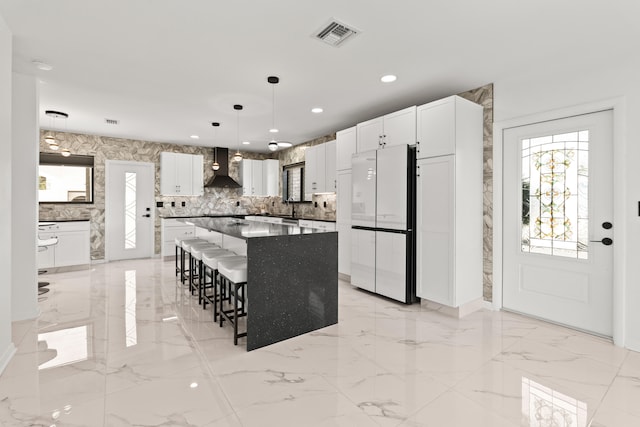 1428 N M St, Lake Worth Beach, FL 33460 - kitchen featuring freestanding refrigerator, wall chimney range hood, light marble finish flooring, a breakfast bar, and recessed lighting