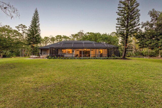 9544 Mockingbird Trl, Jupiter, FL 33478 - back of house at dusk featuring a yard and glass enclosure