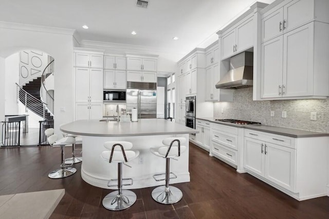 kitchen with built in appliances, exhaust hood, a sink, dark wood finished floors, and ornamental molding