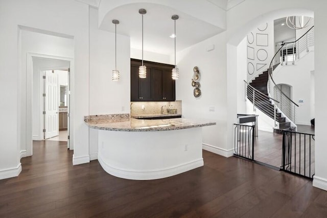 kitchen with dark wood-style floors, dark brown cabinetry, baseboards, light stone counters, and tasteful backsplash