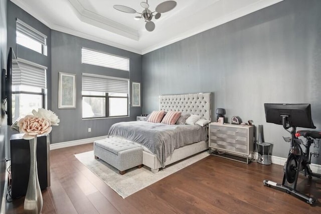 bedroom with a tray ceiling, wood finished floors, crown molding, baseboards, and a ceiling fan