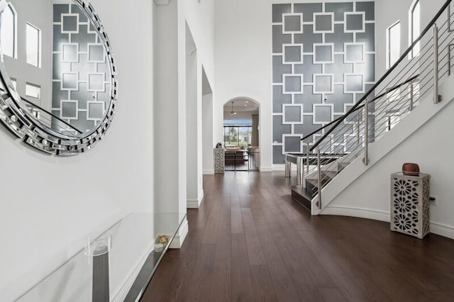 foyer with a towering ceiling, stairs, arched walkways, wood finished floors, and baseboards