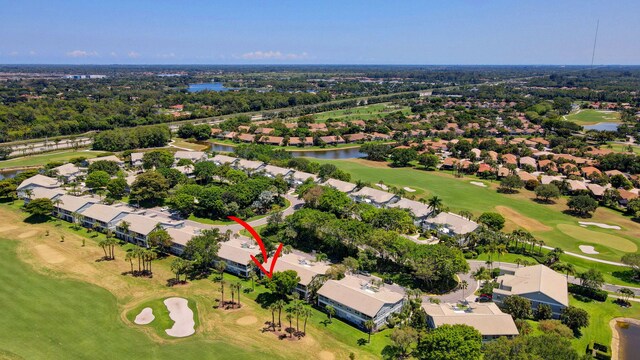 aerial view of property and surrounding area featuring a nearby body of water, a golf course, nearby suburban area, and a tree filled landscape