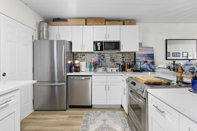 kitchen with stainless steel appliances, white cabinetry, tasteful backsplash, light wood-style floors, and crown molding