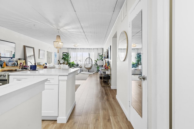 kitchen featuring open floor plan, white cabinetry, light countertops, hanging light fixtures, and light wood-type flooring