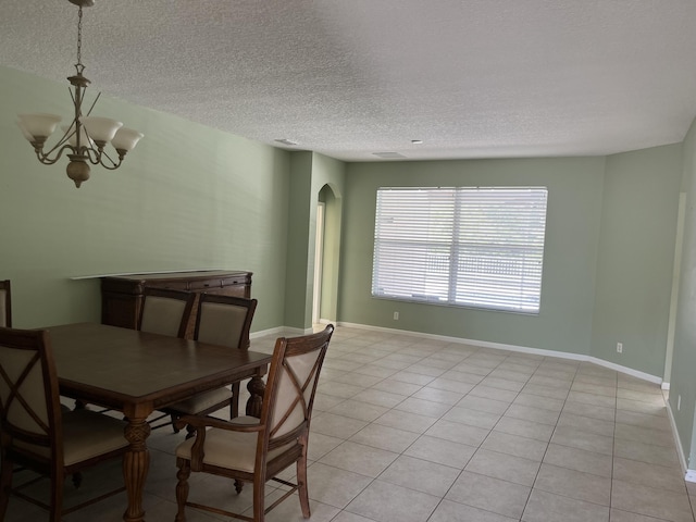6110 46th Ln, Vero Beach, FL 32967 - dining area featuring a chandelier, arched walkways, a textured ceiling, light tile patterned floors, and baseboards
