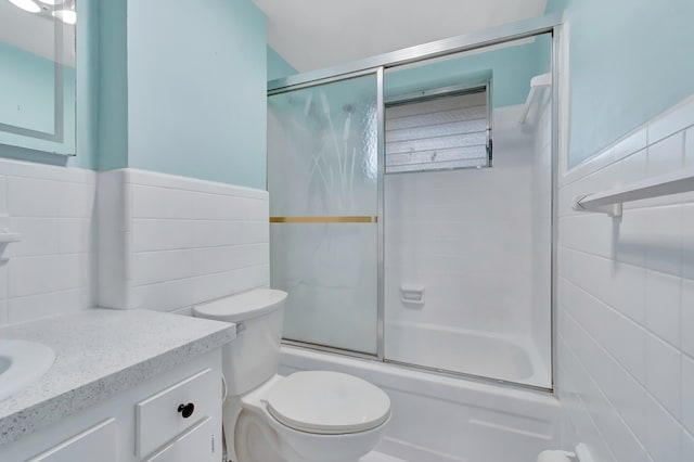 2161 NE 42nd Ct Unit 116, Lighthouse Point, FL 33064 - bathroom featuring tile walls, combined bath / shower with glass door, vanity, toilet, and a wainscoted wall