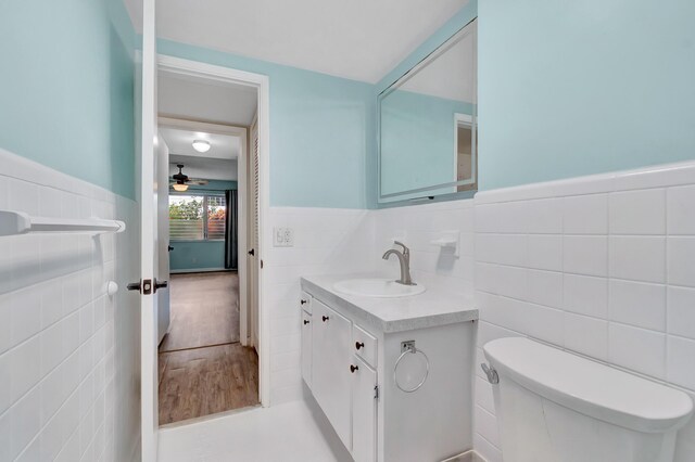 2161 NE 42nd Ct Unit 116, Lighthouse Point, FL 33064 - bathroom with tile walls, toilet, vanity, a wainscoted wall, and ceiling fan
