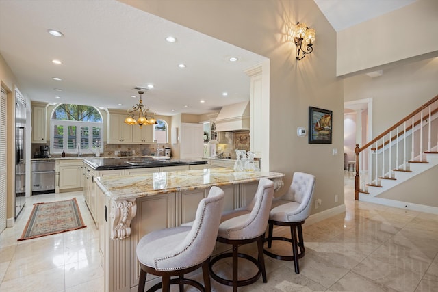 2 Firestone Cir, West Palm Beach, FL 33401 - kitchen featuring recessed lighting, cream cabinetry, custom range hood, tasteful backsplash, and a chandelier