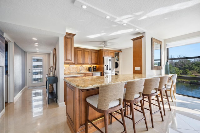 1627 Riverview Rd Unit 409, Deerfield Beach, FL 33441 - kitchen featuring stainless steel fridge with ice dispenser, a textured ceiling, brown cabinetry, light stone countertops, and light tile patterned floors