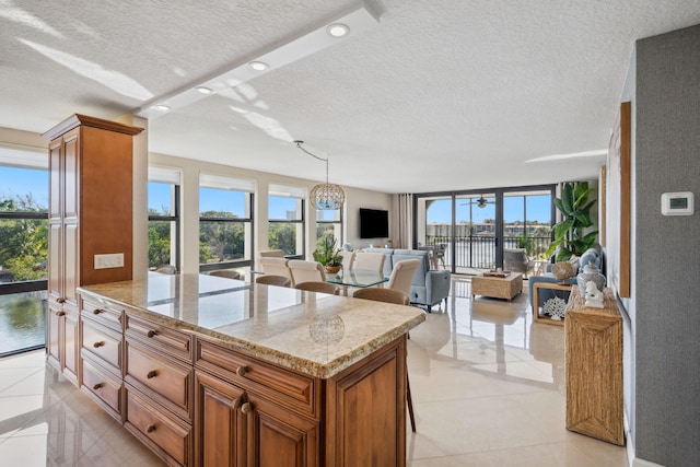 1627 Riverview Rd Unit 409, Deerfield Beach, FL 33441 - kitchen with brown cabinets, a textured ceiling, open floor plan, light stone countertops, and light tile patterned flooring