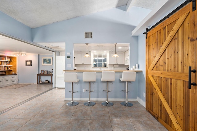 2560 50th Ave, Vero Beach, FL 32966 - kitchen featuring a barn door, light tile patterned flooring, white cabinetry, and a kitchen bar