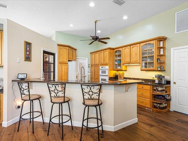 6575 NW Pomona Ct, Port Saint Lucie, FL 34983 - kitchen with open shelves, white appliances, brown cabinets, a kitchen breakfast bar, and a peninsula