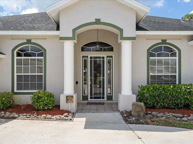 6575 NW Pomona Ct, Port Saint Lucie, FL 34983 - view of exterior entry featuring a shingled roof and stucco siding
