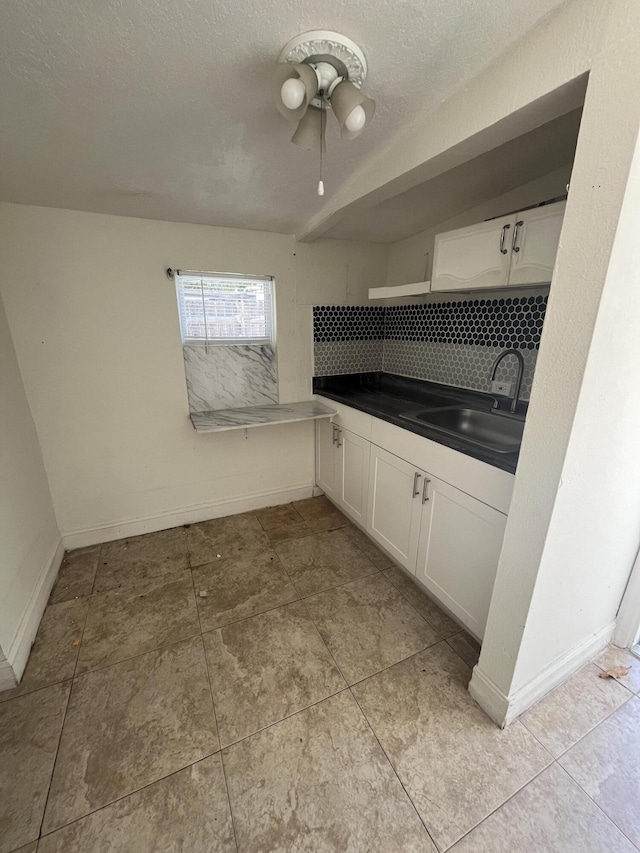 711 Fernwood Dr, West Palm Beach, FL 33405 - kitchen featuring a sink, backsplash, white cabinetry, dark countertops, and baseboards