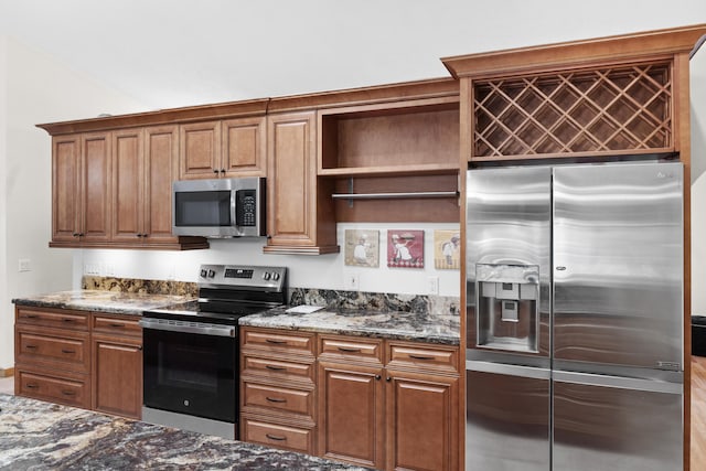kitchen with appliances with stainless steel finishes, dark stone countertops, brown cabinetry, and open shelves