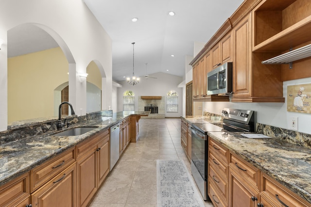 kitchen with appliances with stainless steel finishes, a sink, brown cabinets, dark stone counters, and recessed lighting
