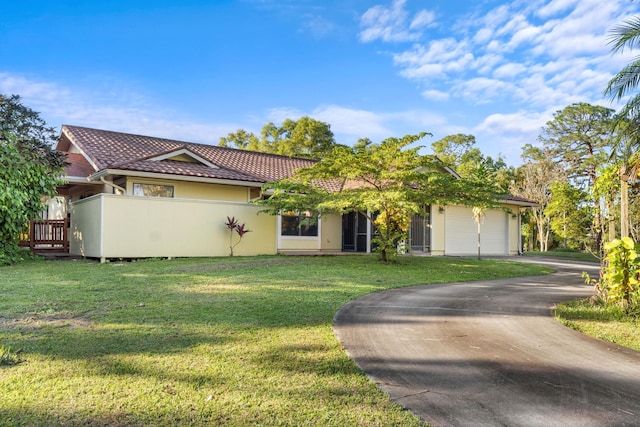 view of front of property featuring a tile roof, asphalt driveway, an attached garage, a front lawn, and stucco siding
