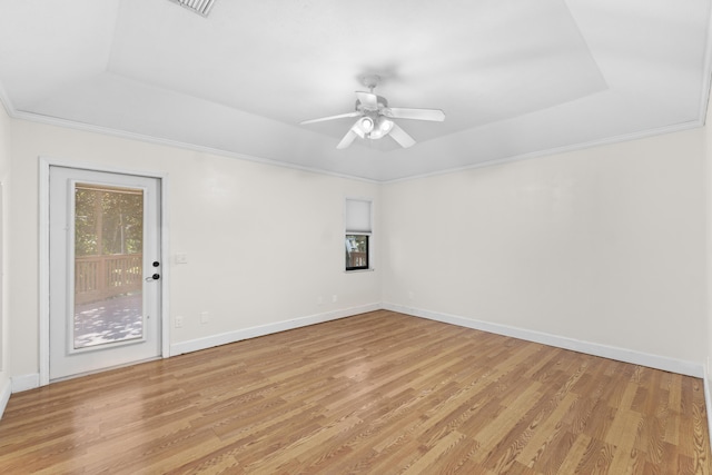 spare room featuring a raised ceiling, light wood finished floors, ceiling fan, and baseboards