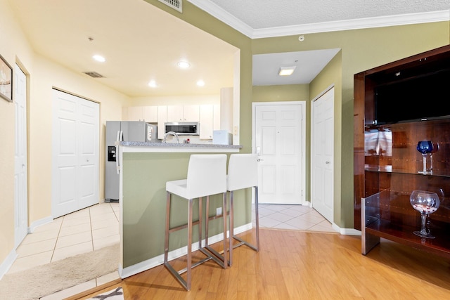 1801 N Flagler Dr Unit 931, West Palm Beach, FL 33407 - kitchen featuring stainless steel microwave, refrigerator with ice dispenser, white cabinets, a kitchen breakfast bar, and light wood finished floors
