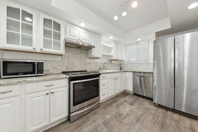 3186 Via Poinciana Unit 115, Lake Worth, FL 33467 - kitchen with stainless steel appliances, under cabinet range hood, a sink, glass insert cabinets, and decorative backsplash