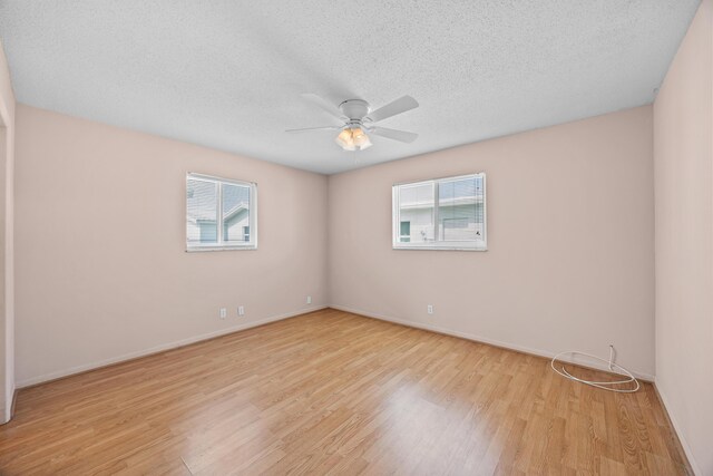 empty room with plenty of natural light, light wood finished floors, ceiling fan, baseboards, and a textured ceiling