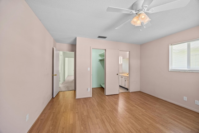unfurnished bedroom featuring a walk in closet, light wood-type flooring, a closet, baseboards, and a ceiling fan