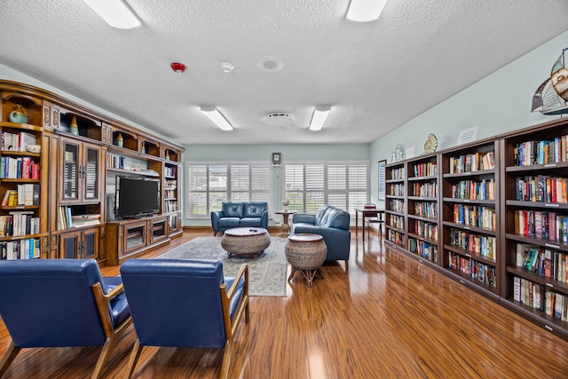 living area with wall of books, a textured ceiling, and wood finished floors