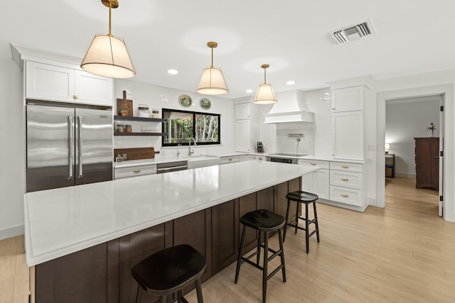 4972 S Kay St, Palm Beach Gardens, FL 33418 - kitchen featuring stainless steel appliances, custom range hood, a sink, light countertops, and white cabinets