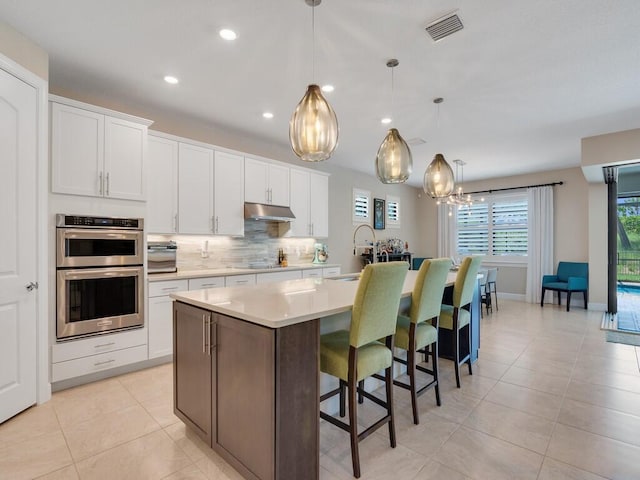 5082 Monroe Cir, Vero Beach, FL 32967 - kitchen with an island with sink, decorative backsplash, stainless steel double oven, light countertops, and light tile patterned flooring