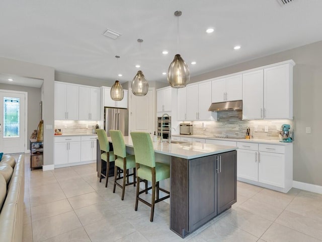 5082 Monroe Cir, Vero Beach, FL 32967 - kitchen with under cabinet range hood, appliances with stainless steel finishes, decorative backsplash, light countertops, and white cabinetry