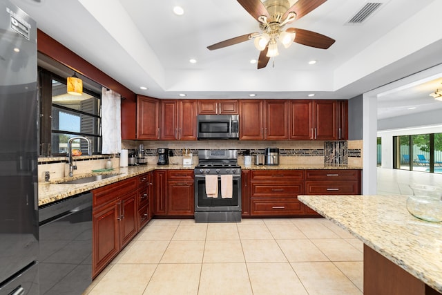kitchen featuring stainless steel appliances, a sink, backsplash, reddish brown cabinets, and light stone counters